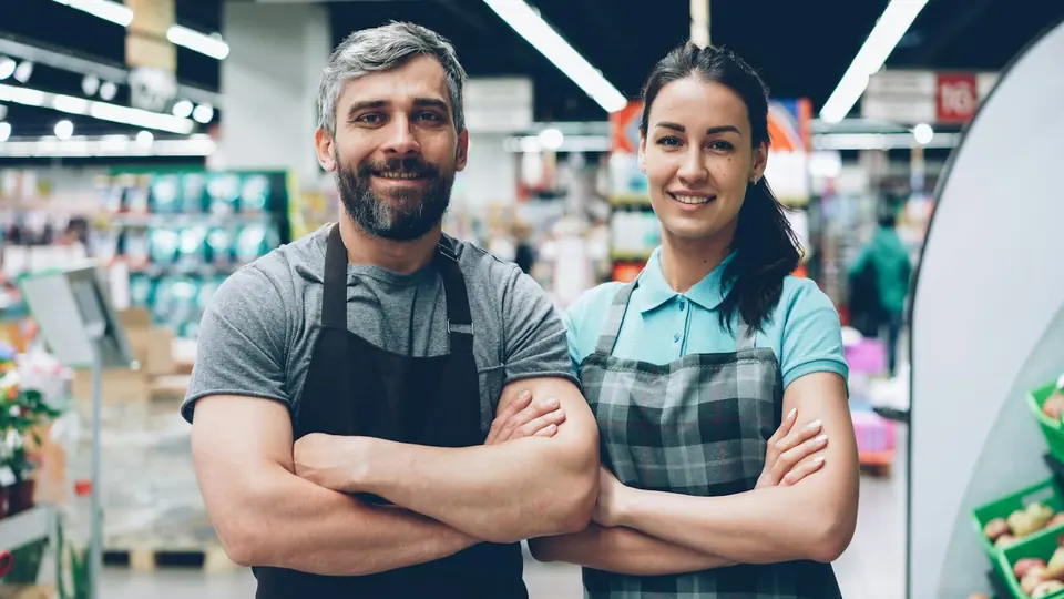 Verkäufer und Verkäuferin mit Schürzen im Supermarkt, lächelnd