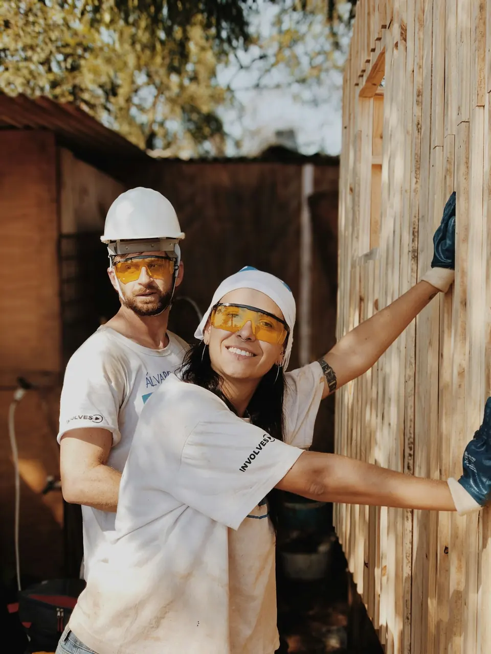 Handwerkerin und Handwerker mit Helm und Schutzbrille vor Holzwand