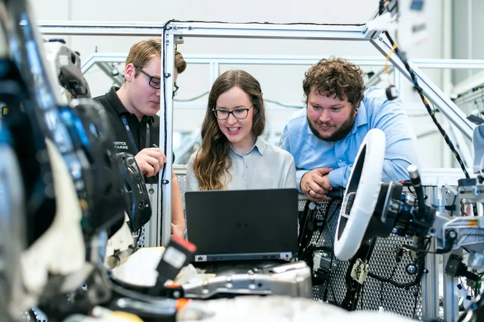 Ingenieurin und zwei Kollegen an Maschine mit Laptop, lachend