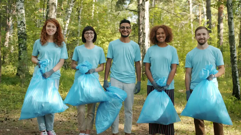 Putz- und Aufräumteam in hellblauen Shirts mit Müllsäcken, lächelnd