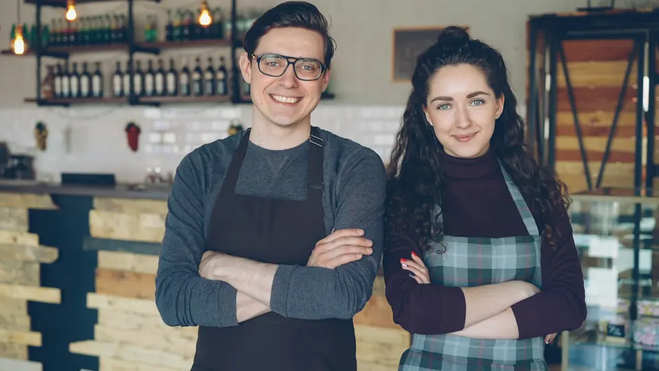 Zwei Kollegen mit Schürze in Restaurant/Bar, lächelnd